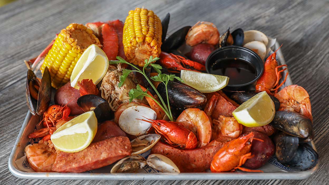 A tray filled with a variety of seafood including lobster, prawns, mussels, clams, and corn on the cob, garnished with lemon wedges and parsley, ready for a feast.